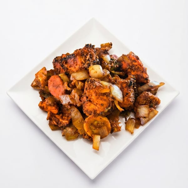 Spicy chicken tikka with onions and carrots on a white square plate.